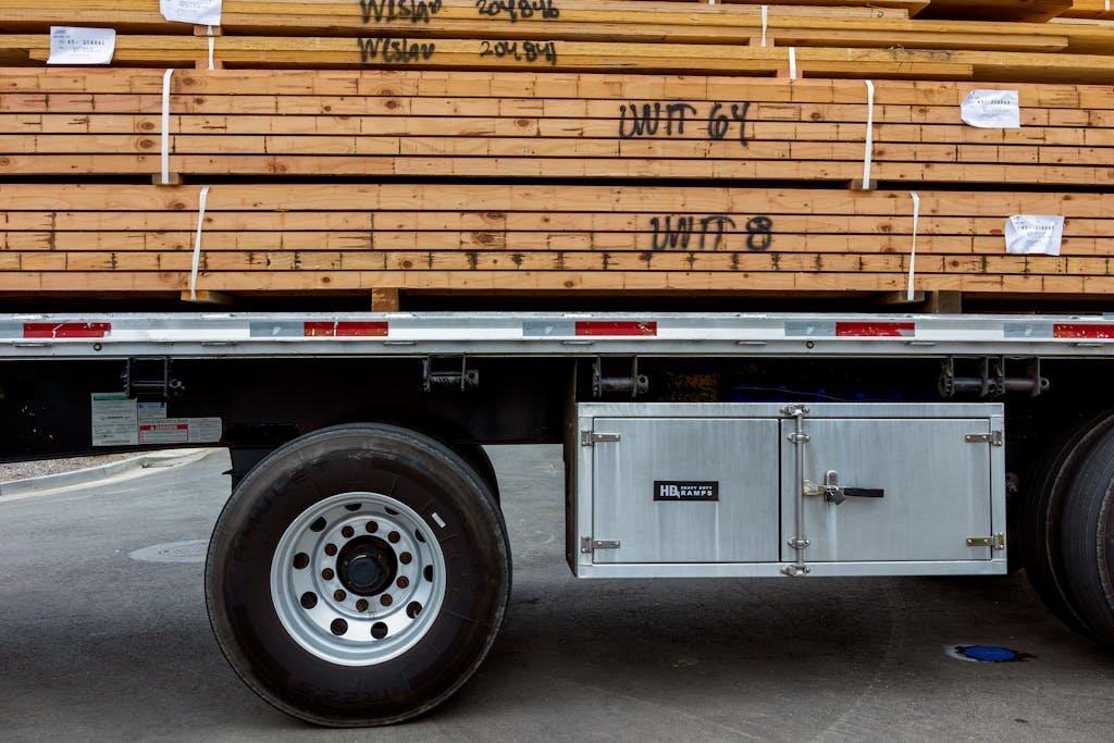 A large stack of wooden planks loaded onto an industrial trailer in an outdoor setting.